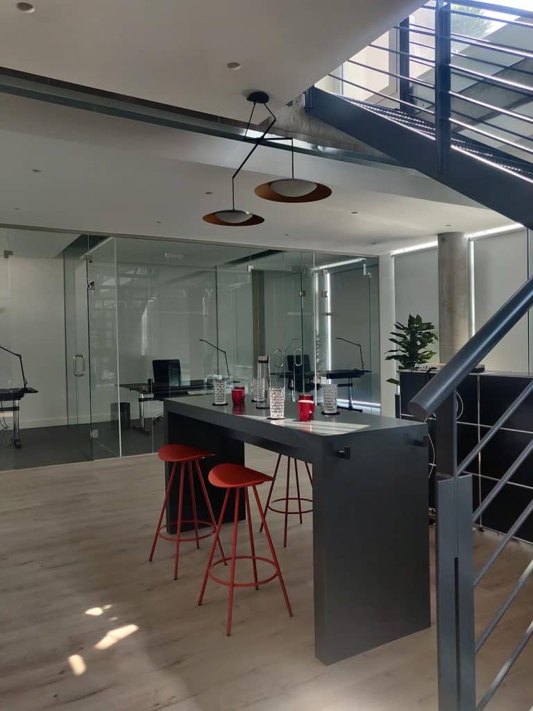 Barra alta con taburetes rojos junto a la escalera en las oficinas de Majadahonda