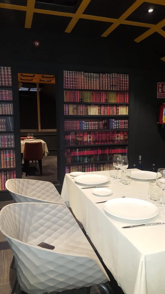 Comedor del restaurante D'Sexto con librería al fondo y sillas blancas