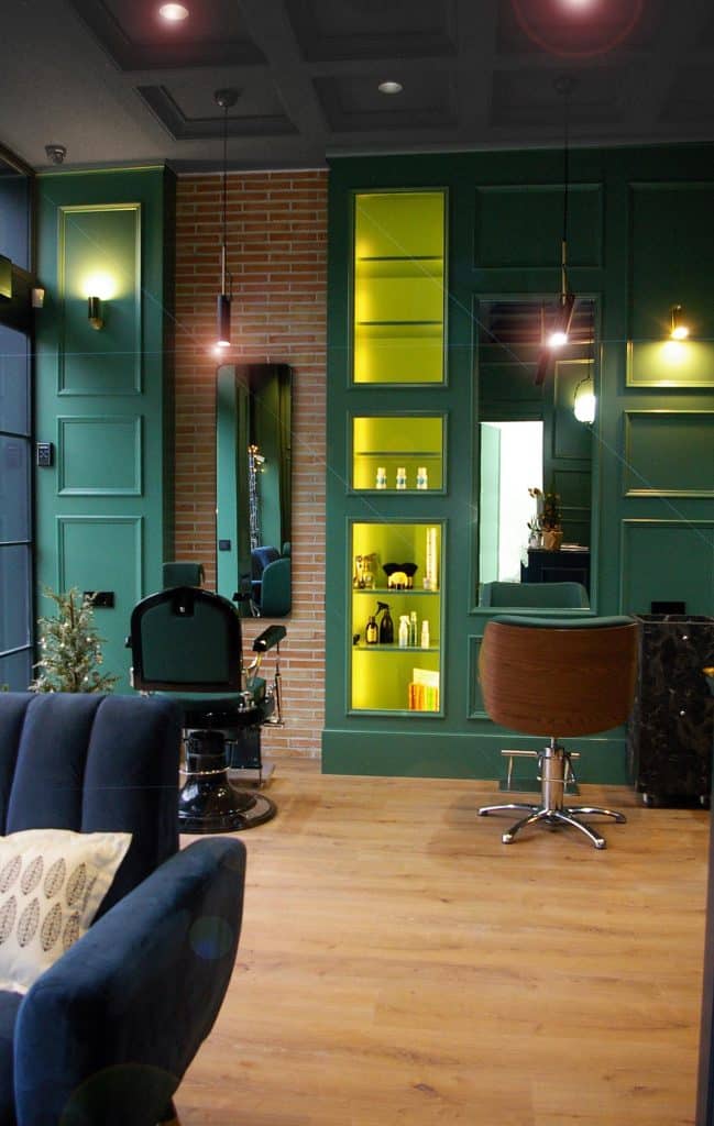 Zona de tocadores con paredes verdes y vitrinas iluminadas en el salón de belleza Cociu
