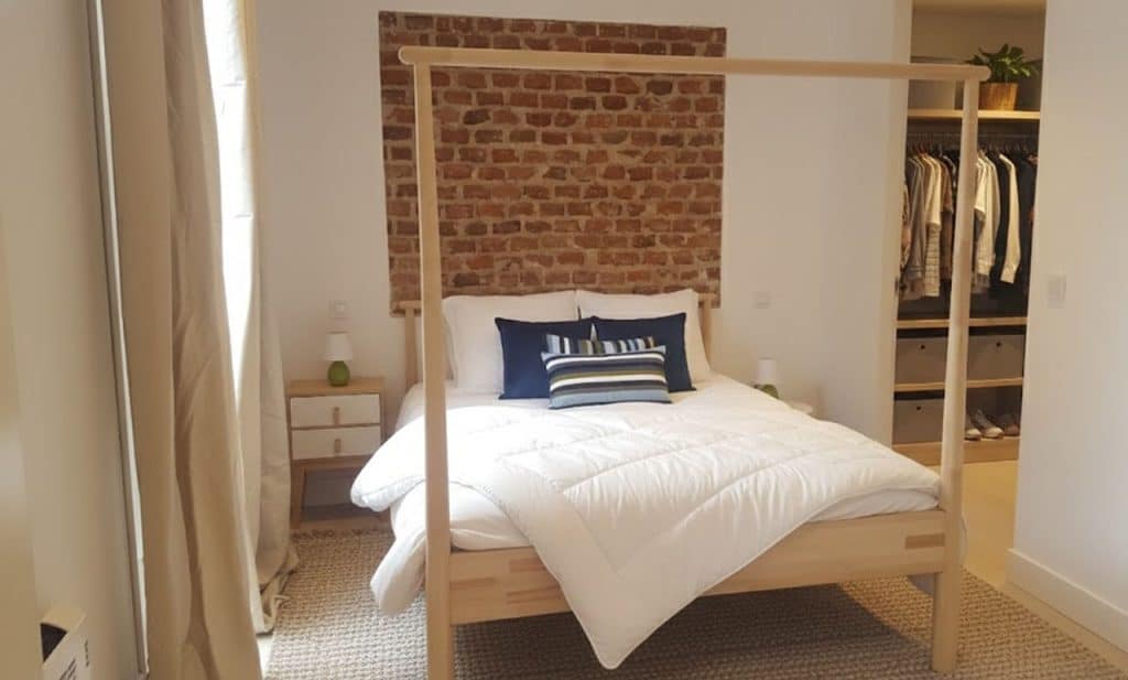 Dormitorio con cama con dosel de madera y pared de ladrillo visto junto a Madrid Río