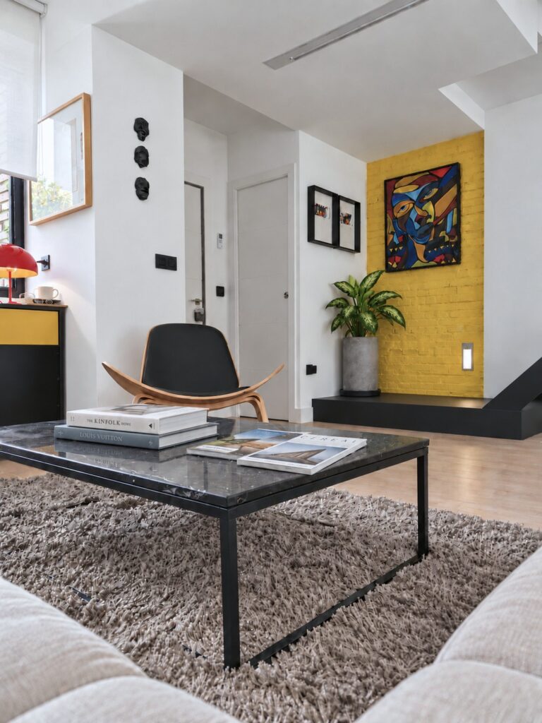 Salón con mesa de centro negra, butaca de madera y pared amarilla en la casa-estudio de Las Matas