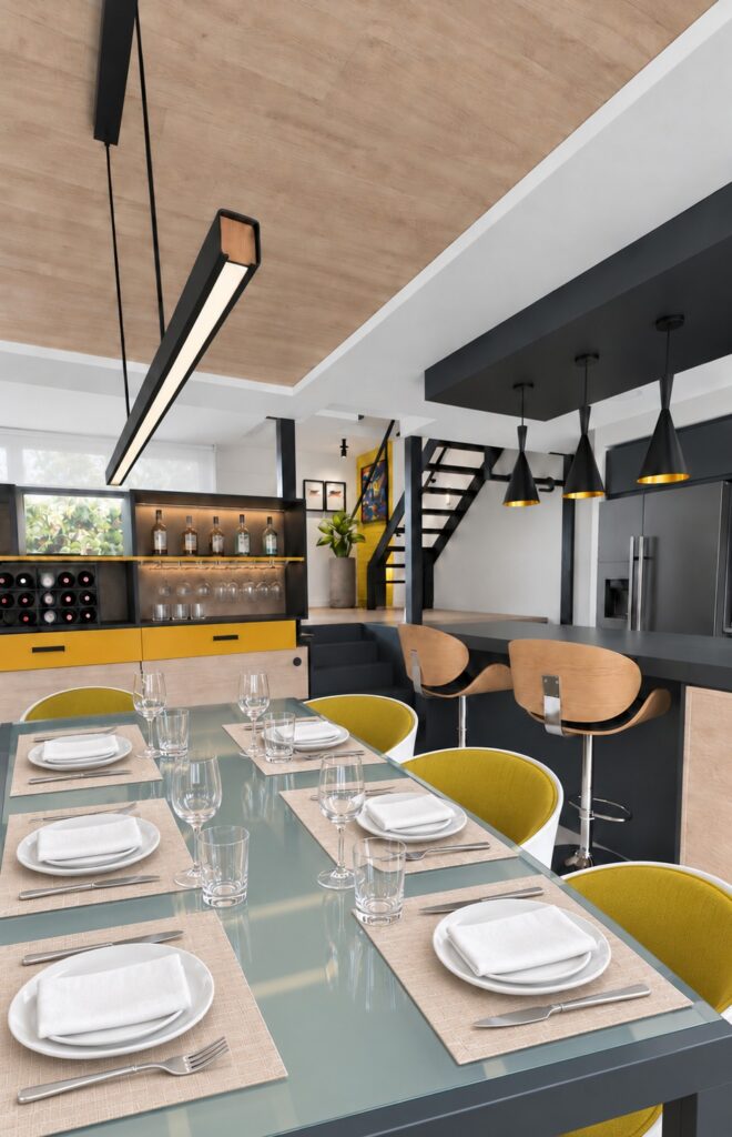 Mesa de comedor de vidrio con sillas amarillas y cocina negra al fondo en la casa-estudio de Las Matas