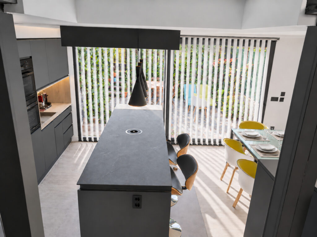 Cocina negra con isla y ventanal con estor vertical hacia el jardín en la casa-estudio de Las Matas